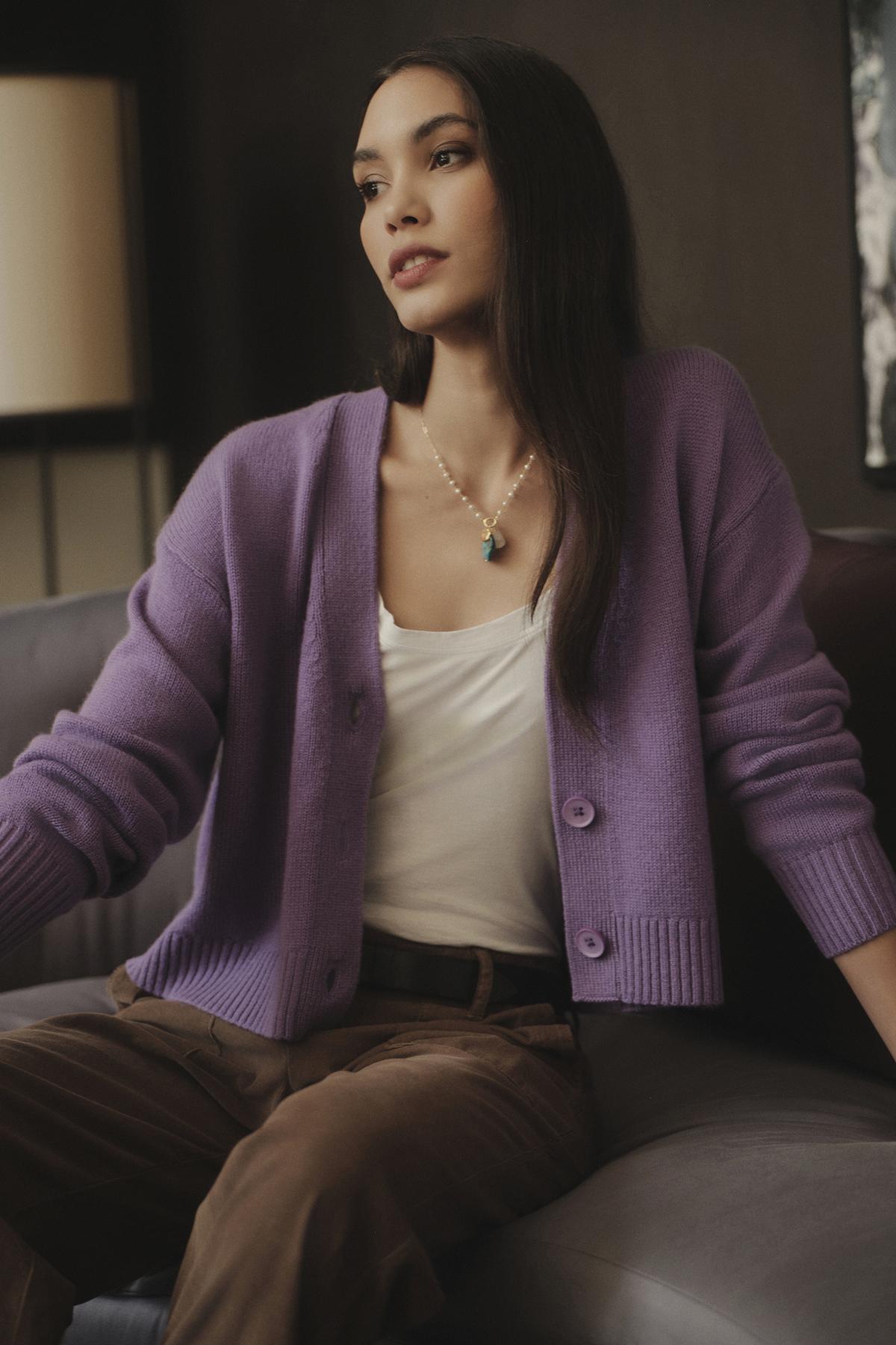 A woman is sitting on a couch wearing a Velvet by Graham & Spencer CHARLI WOOL CASHMERE CARDIGAN.-26921631809729