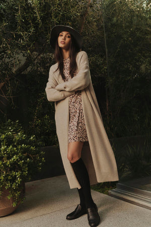 A woman in a beige coat and hat is posing for a photo, showcasing the elegant neckline of her Velvet by Graham & Spencer GENE PRINTED TIERED DRESS.