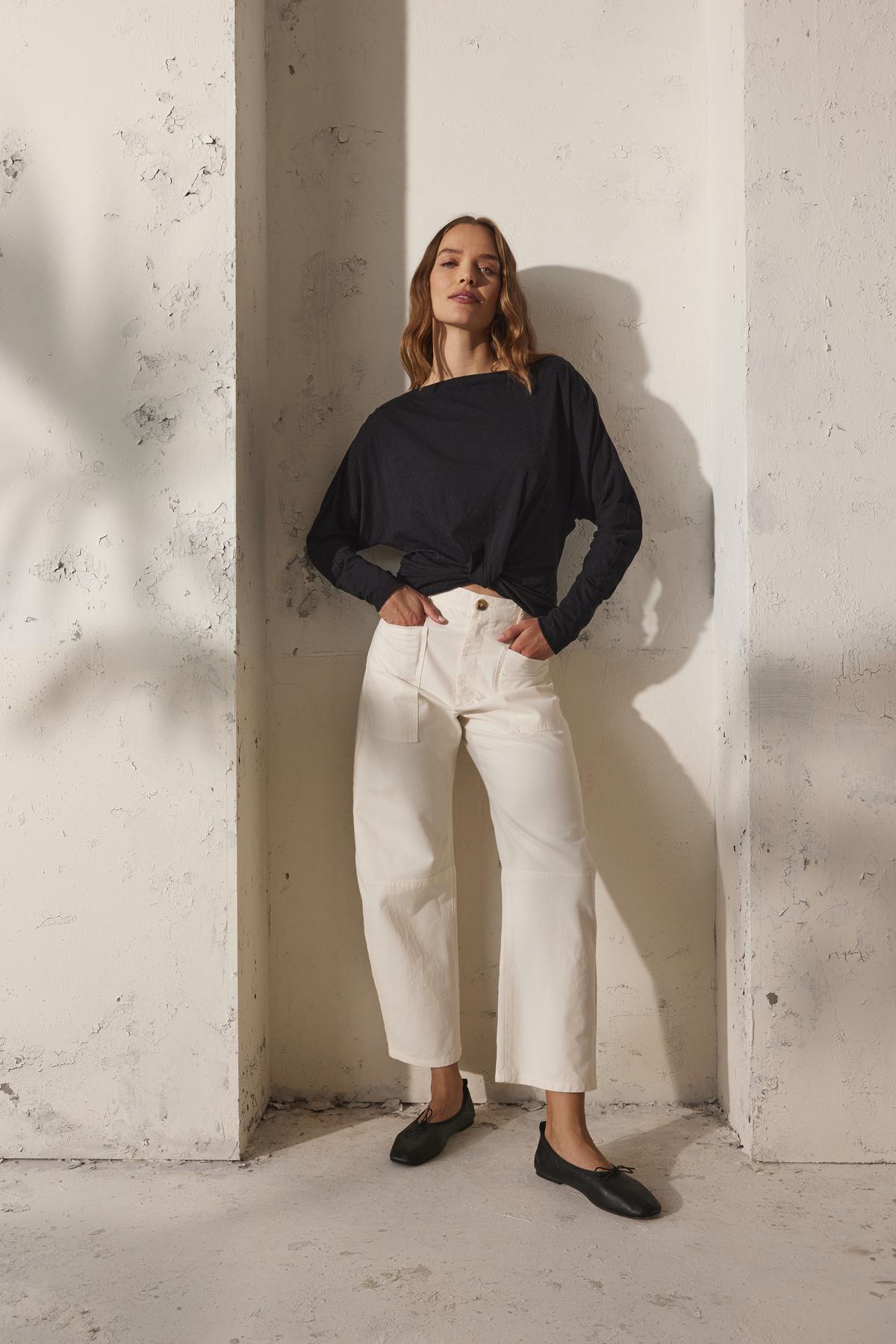   Against a textured white wall, a person wears a black long-sleeve shirt, the BRYLIE SANDED TWILL UTILITY PANT by Velvet by Graham & Spencer, and black shoes. 