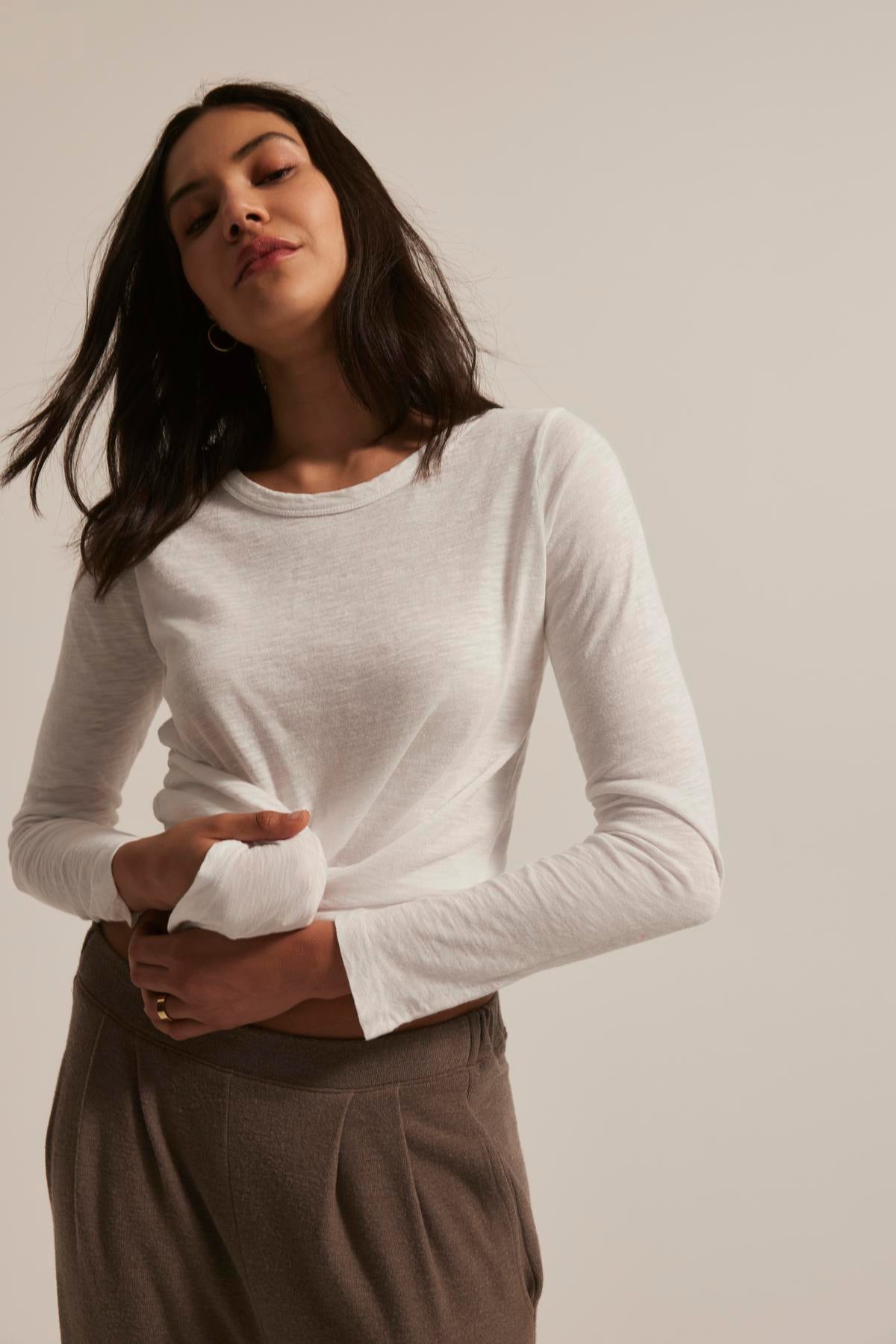 A woman poses against a plain background wearing the LIZZIE TEE by Velvet by Graham & Spencer, a textured cotton slub long-sleeve shirt with a classic crew neckline, paired with brown pants.-38433356611777