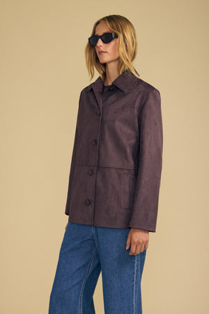 Wearing the WENDOLYN FAUX SUEDE JACKET by Velvet by Graham & Spencer, a woman in blue jeans and black sunglasses stands against a plain beige background.