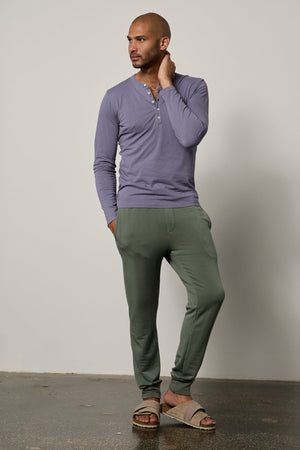 a man is posing in a green Velvet by Graham & Spencer ALVARO COTTON JERSEY HENLEY tee and sweatpants.