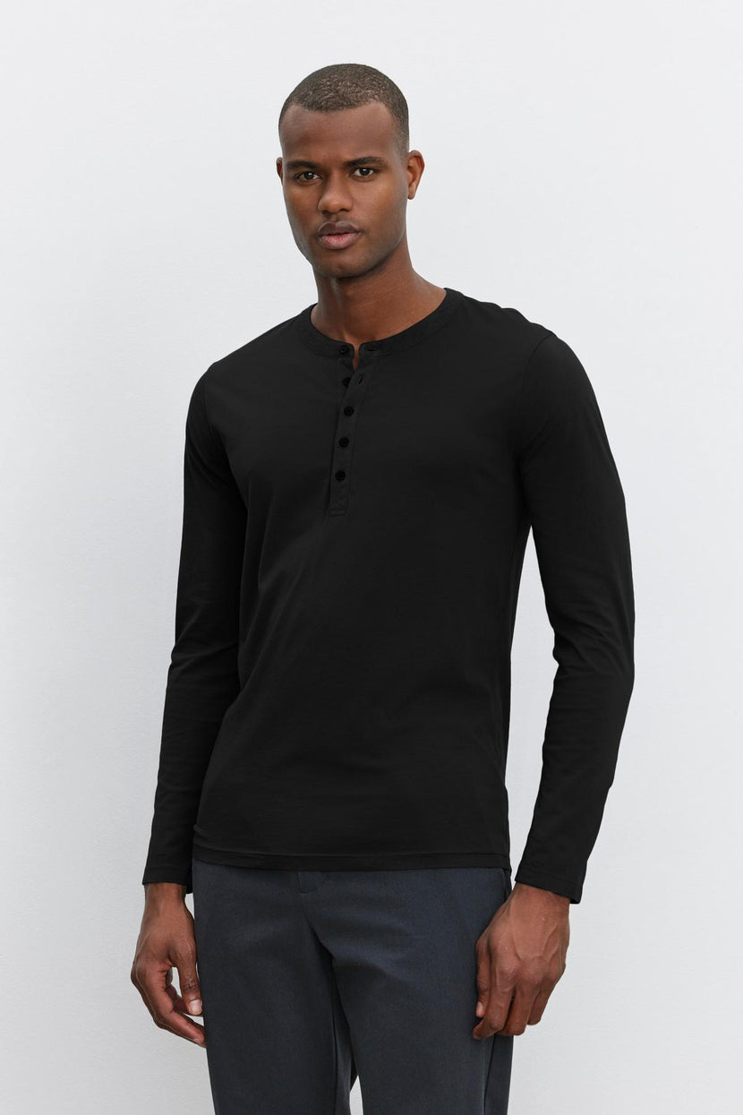 A person is standing against a plain background, wearing a black long-sleeve lightweight ALVARO HENLEY by Velvet by Graham & Spencer and dark jeans.