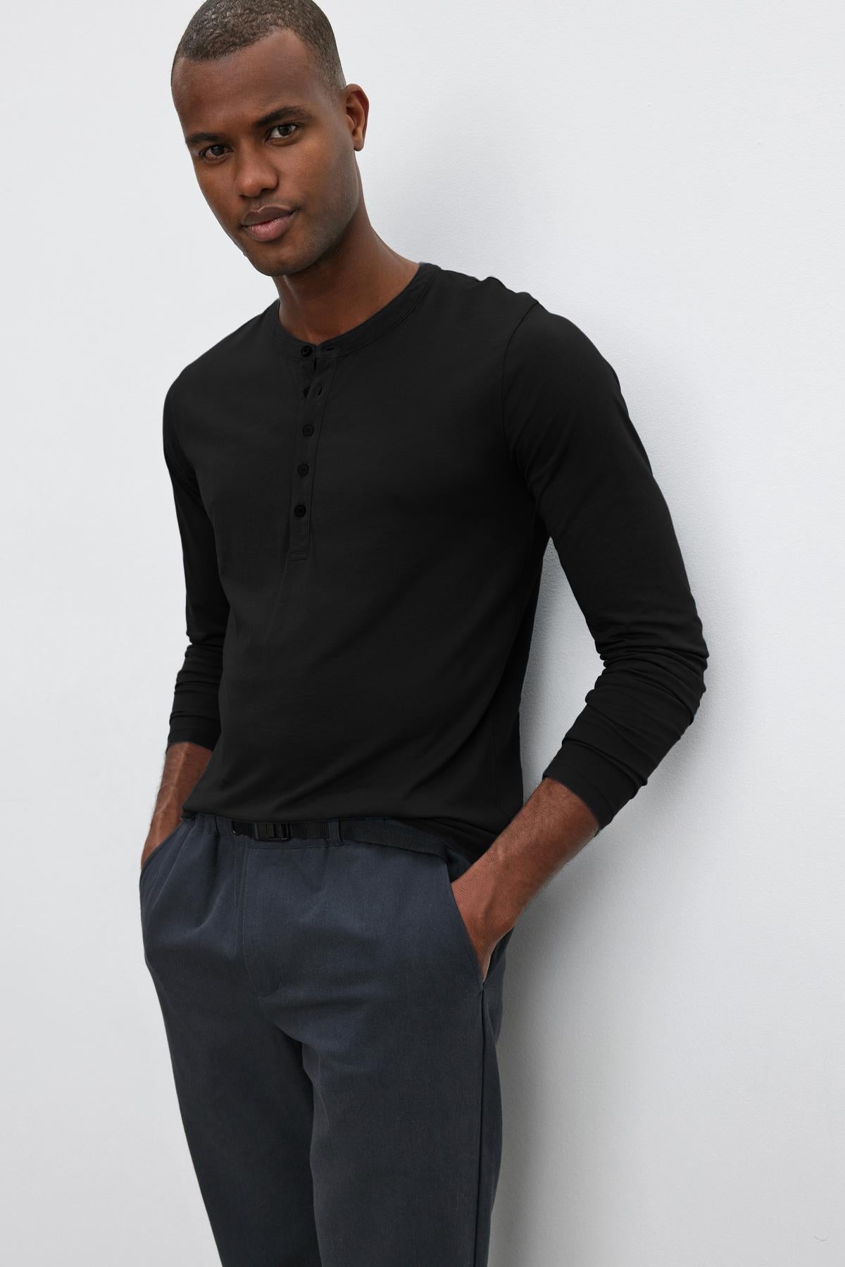   A man wearing a Velvet by Graham & Spencer ALVARO COTTON JERSEY HENLEY leans against a wall. 