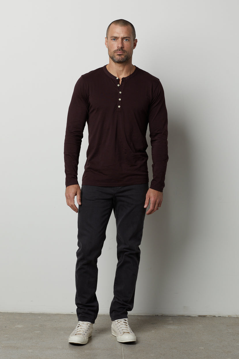 A man wearing a lightweight Alvaro Cotton Jersey Henley shirt by Velvet by Graham & Spencer and vintage-look black pants.