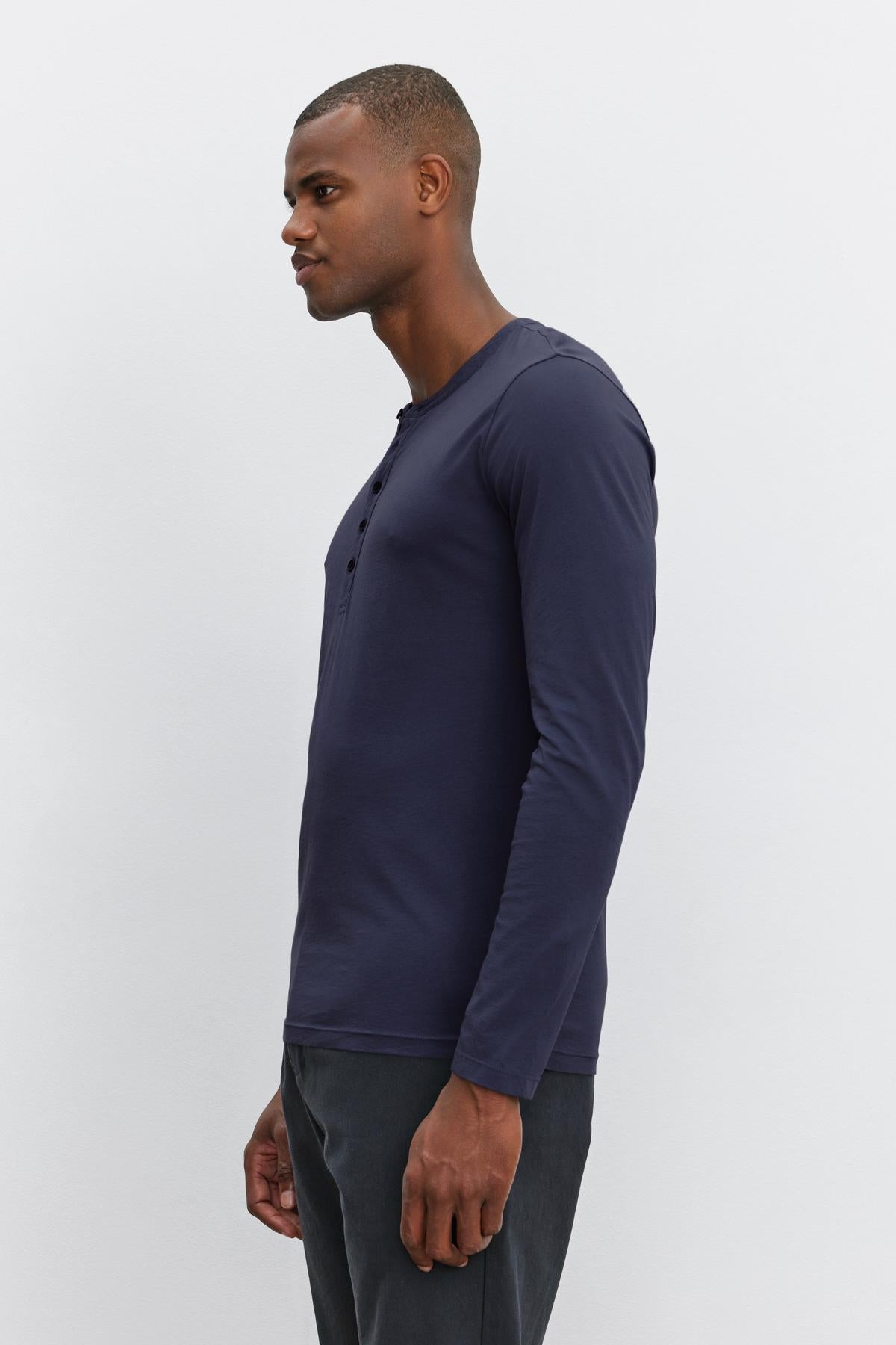   The man is wearing a lightweight navy ALVARO COTTON JERSEY HENLEY long-sleeved t-shirt by Velvet by Graham & Spencer. 