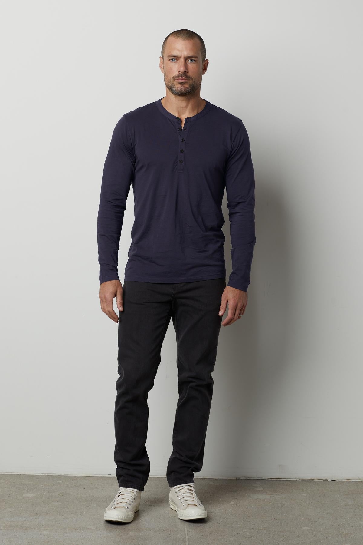 A man wearing a soft navy ALVARO COTTON JERSEY HENLEY t-shirt and lightweight black pants by Velvet by Graham & Spencer.-35607611113665
