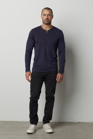 A man wearing a soft navy ALVARO COTTON JERSEY HENLEY t-shirt and lightweight black pants by Velvet by Graham & Spencer.