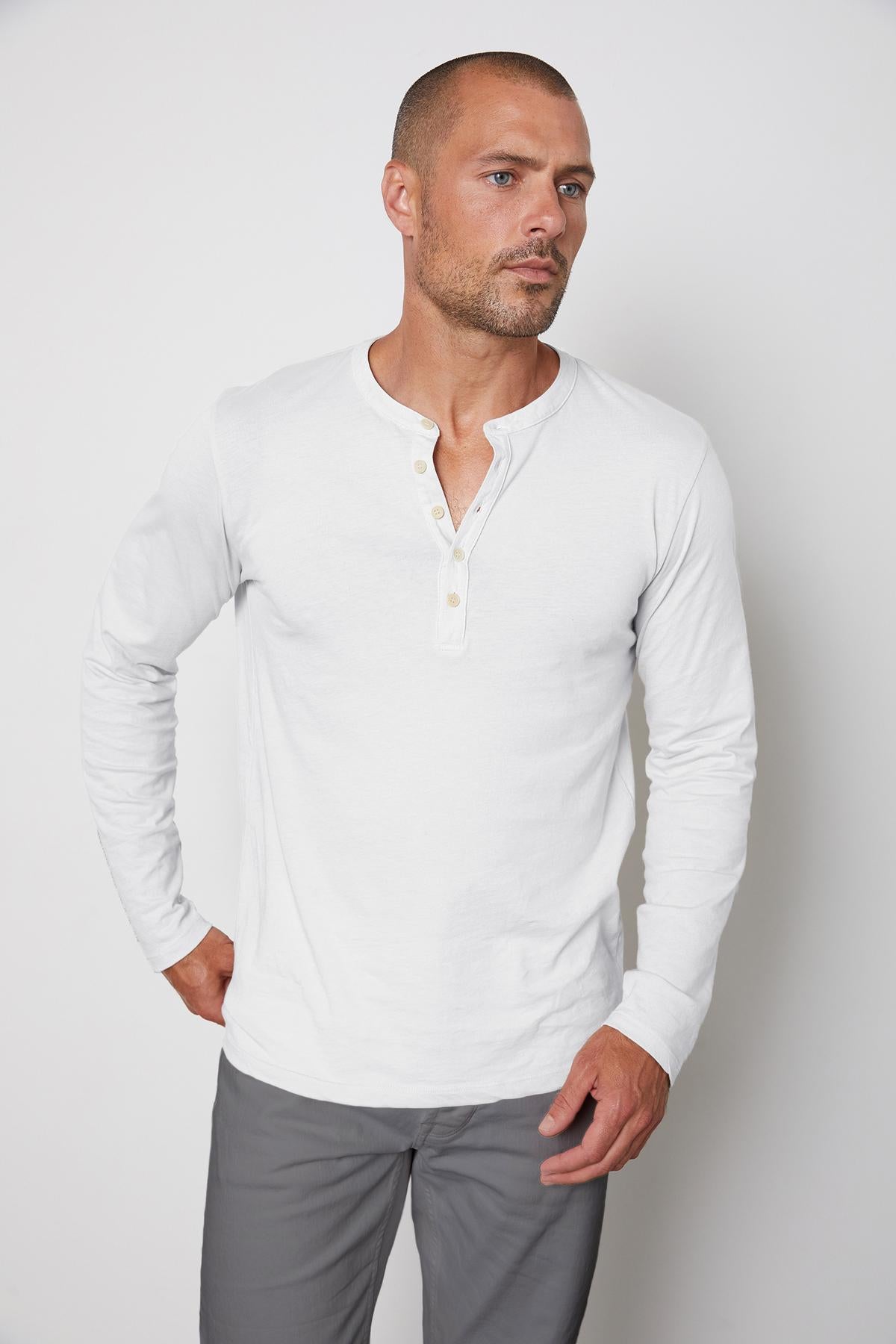 A man wearing a lightweight white Velvet by Graham & Spencer ALVARO COTTON JERSEY HENLEY shirt and gray pants.-36273890296001