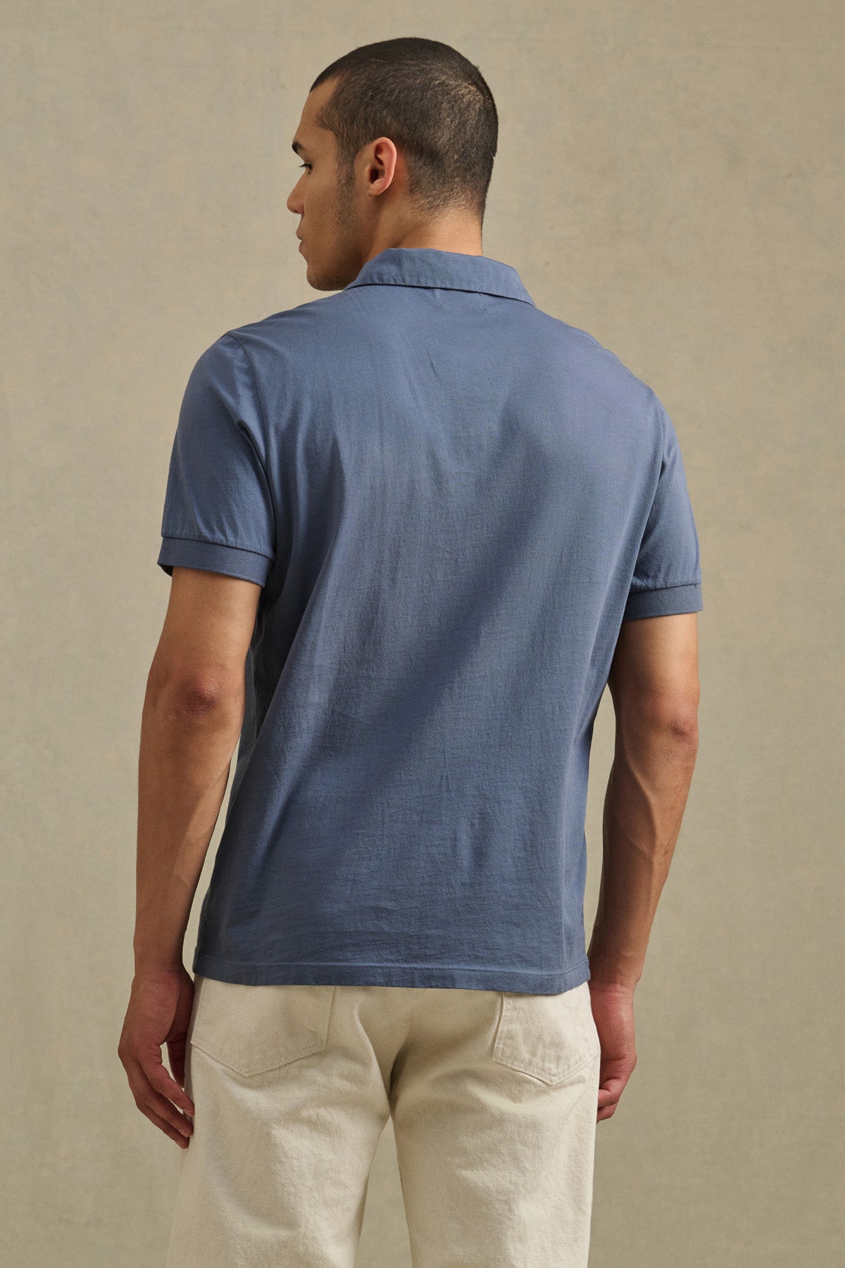 A person faces away wearing the ARROW POLO by Velvet by Graham & Spencer—a classic style, short-sleeve, lightweight blue polo—paired with off-white pants against a plain background.-41104666263745