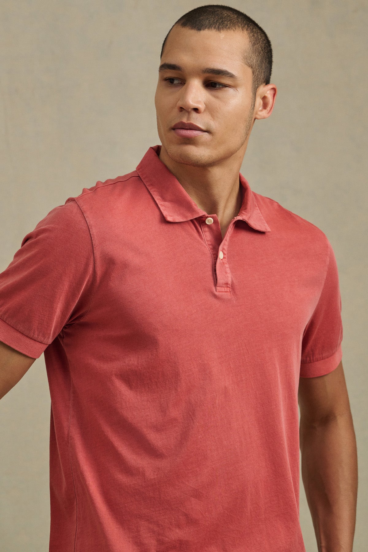 A man wears the ARROW POLO by Velvet by Graham & Spencer in faded red, standing against a plain, light background and looking slightly to his left.