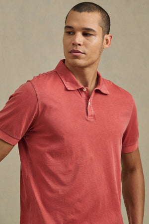 A man wears the ARROW POLO by Velvet by Graham & Spencer in faded red, standing against a plain, light background and looking slightly to his left.