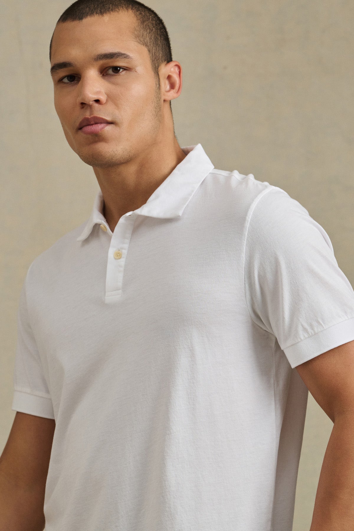 A man models the ARROW POLO by Velvet by Graham & Spencer in white cotton, standing against a neutral background and looking slightly to the side.
