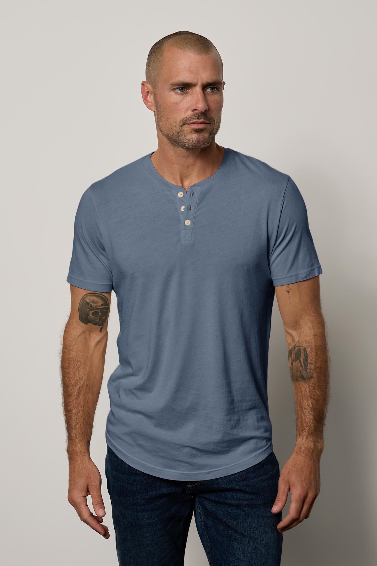A man wearing a blue Velvet by Graham & Spencer Fulton Short Sleeve Henley t-shirt.-35567476998337