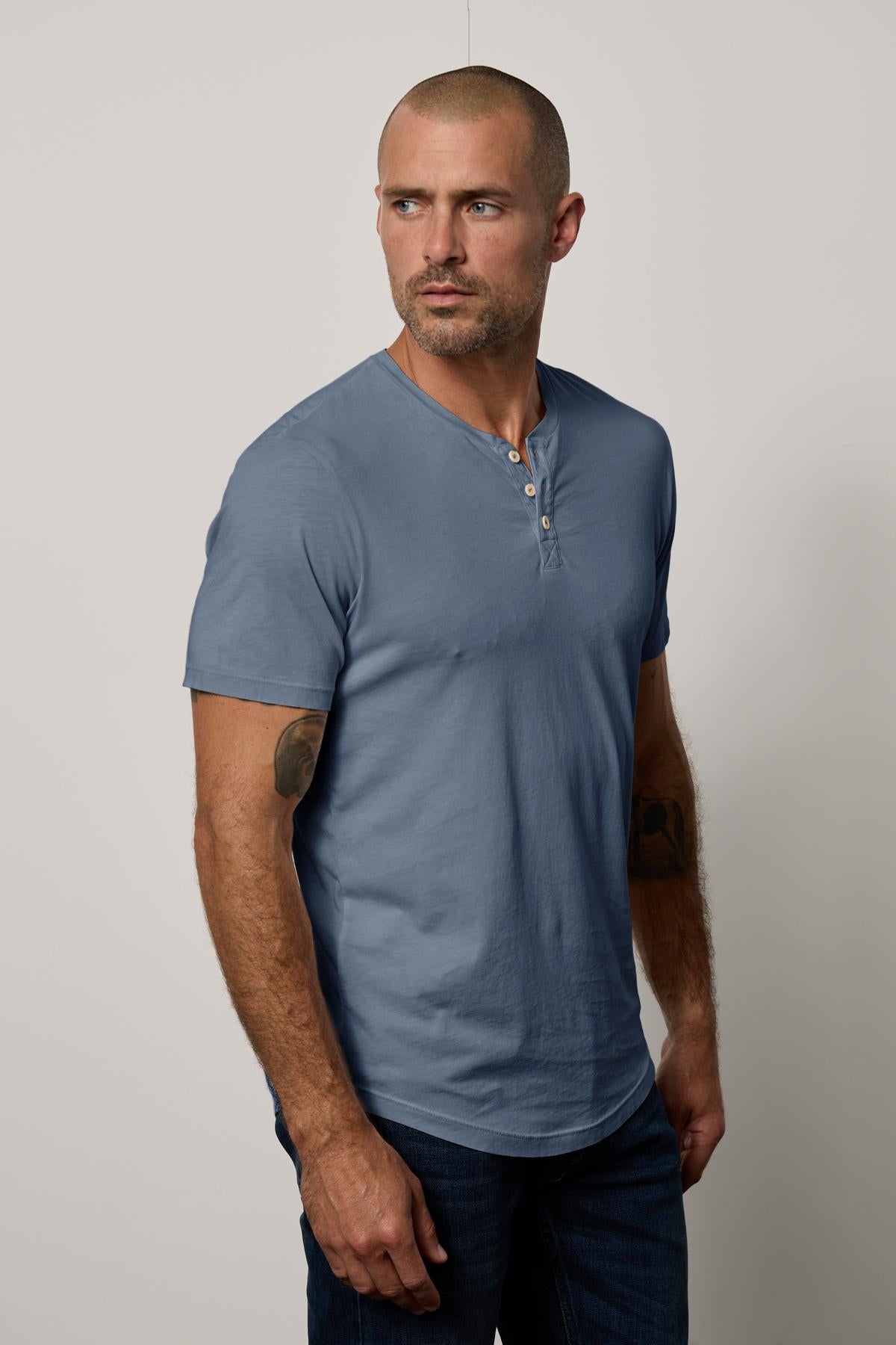   A man wearing a blue Velvet by Graham & Spencer Fulton Short Sleeve Henley t-shirt. 