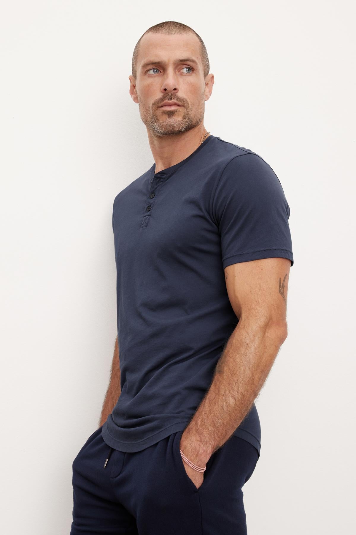   Man in a navy blue Velvet by Graham & Spencer Fulton Henley and pants posing with his hand in his pocket against a white background. 