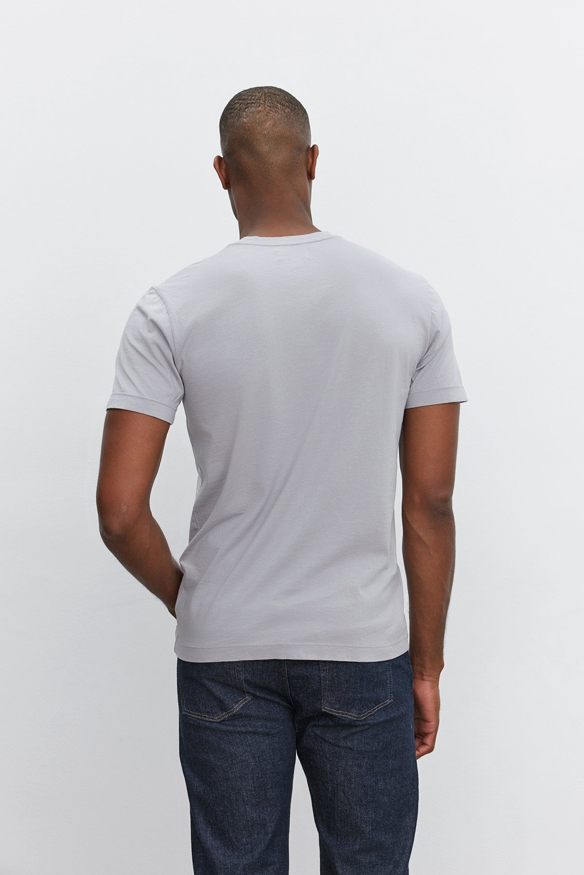   Back view of a person wearing the HOWARD TEE by Velvet by Graham & Spencer, a lightweight cotton knit light gray short-sleeve t-shirt, and dark blue jeans against a plain white background. 