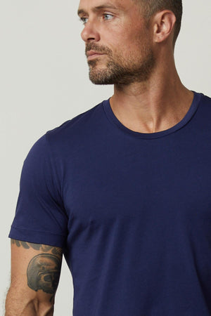 A man with flawless fit wearing a Velvet by Graham & Spencer HOWARD WHISPER CLASSIC CREW NECK TEE adorned with tattoos.