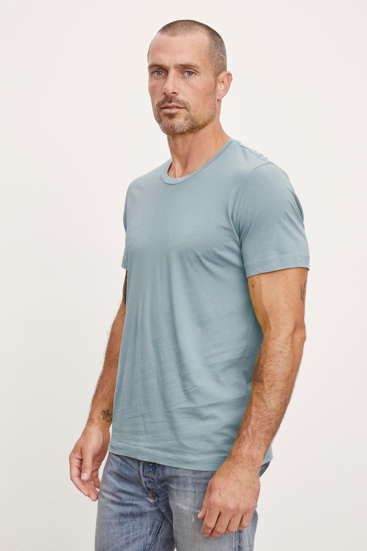   A man wearing a Velvet by Graham & Spencer Howard Whisper Classic Crew Neck Tee in blue and jeans. 