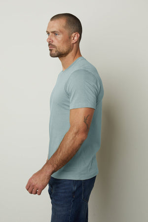 A man wearing a Velvet by Graham & Spencer HOWARD WHISPER CLASSIC CREW NECK TEE made from lightweight cotton knit, with a vintage-feel softness in blue.