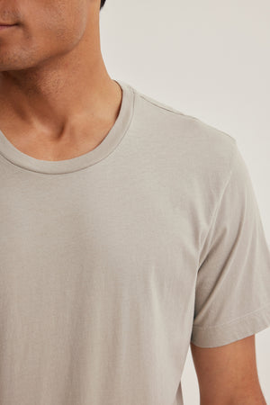 A person is shown from the neck down in a light gray HOWARD TEE by Velvet by Graham & Spencer against a neutral background, giving off a vintage feel.
