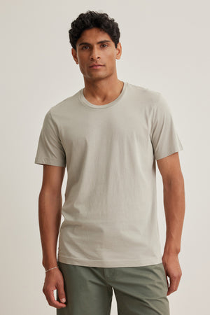 A man with short dark hair wears the Velvet by Graham & Spencer HOWARD TEE in light gray and olive green pants, standing against a plain light background.