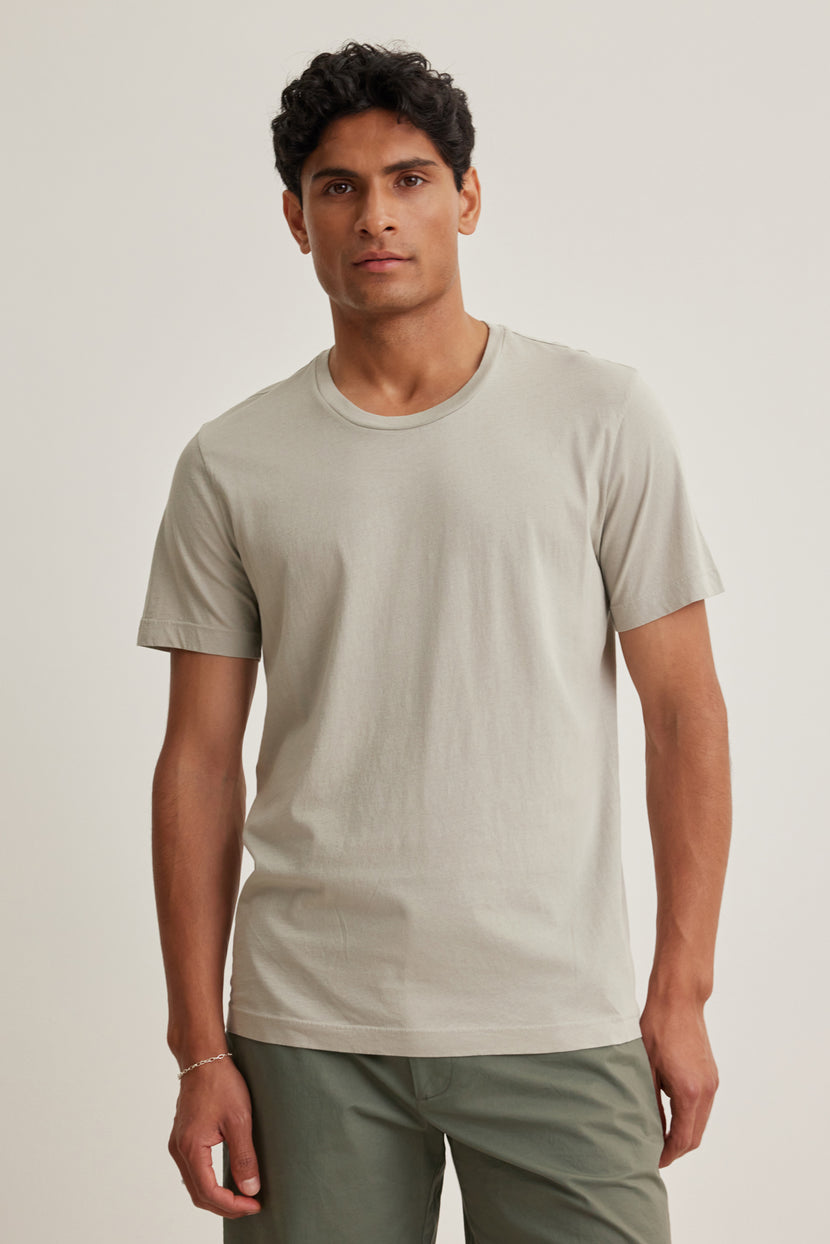 A man with short dark hair wears the Velvet by Graham & Spencer HOWARD TEE in light gray and olive green pants, standing against a plain light background.