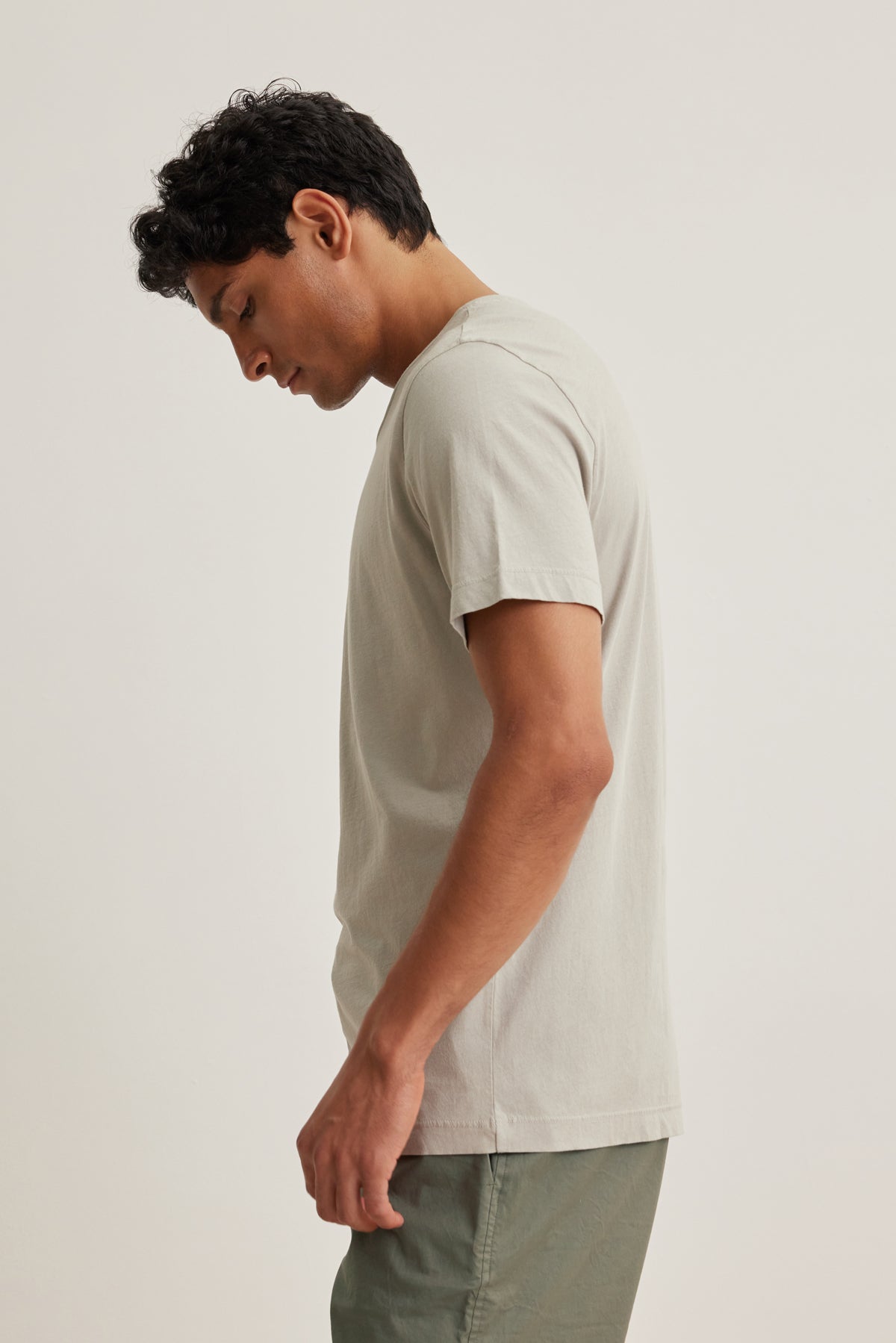   A man stands in profile against a plain background, wearing the HOWARD TEE by Velvet by Graham & Spencer, a light-colored t-shirt made from lightweight Pima jersey for a perfect fit, paired with green pants. 