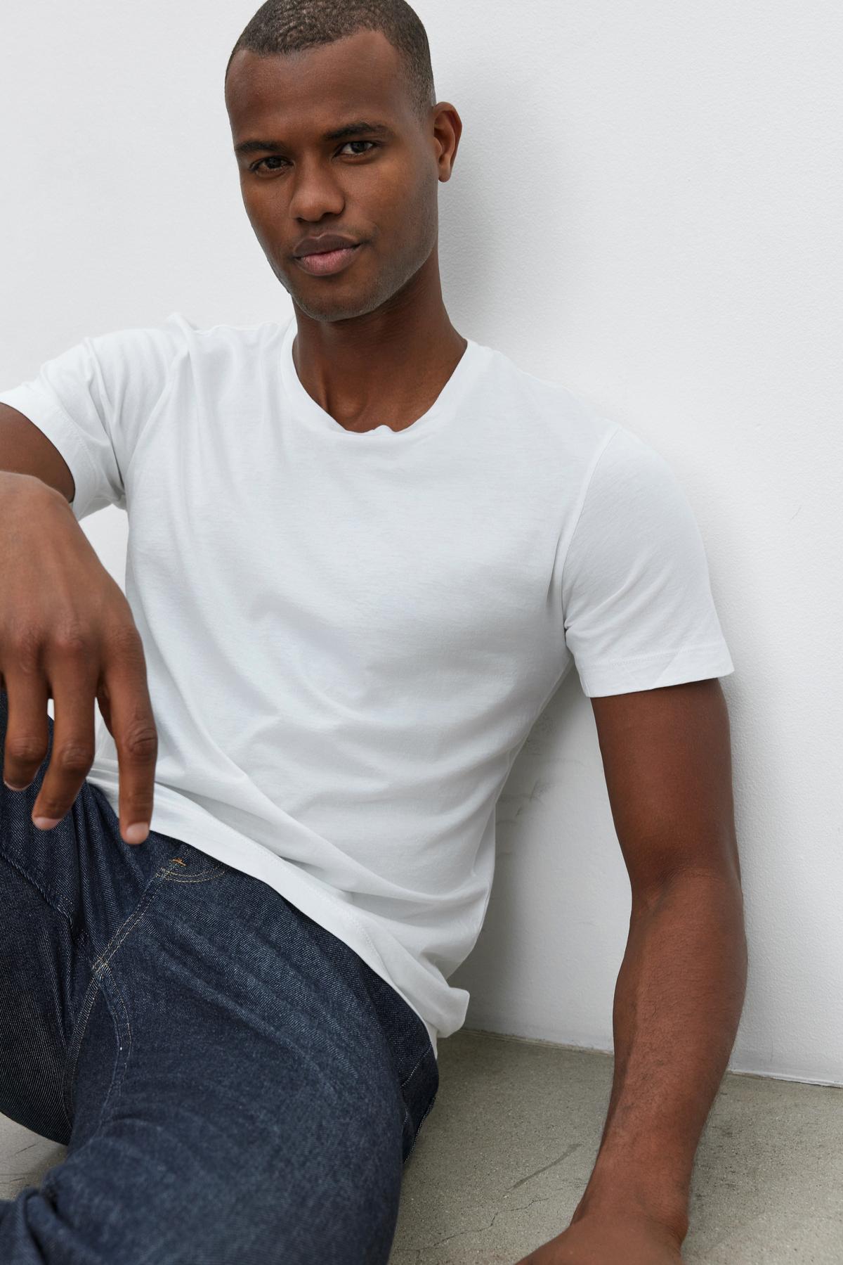 A man in a Velvet by Graham & Spencer HOWARD WHISPER CLASSIC CREW NECK TEE, leaning against a wall.-35867473150145