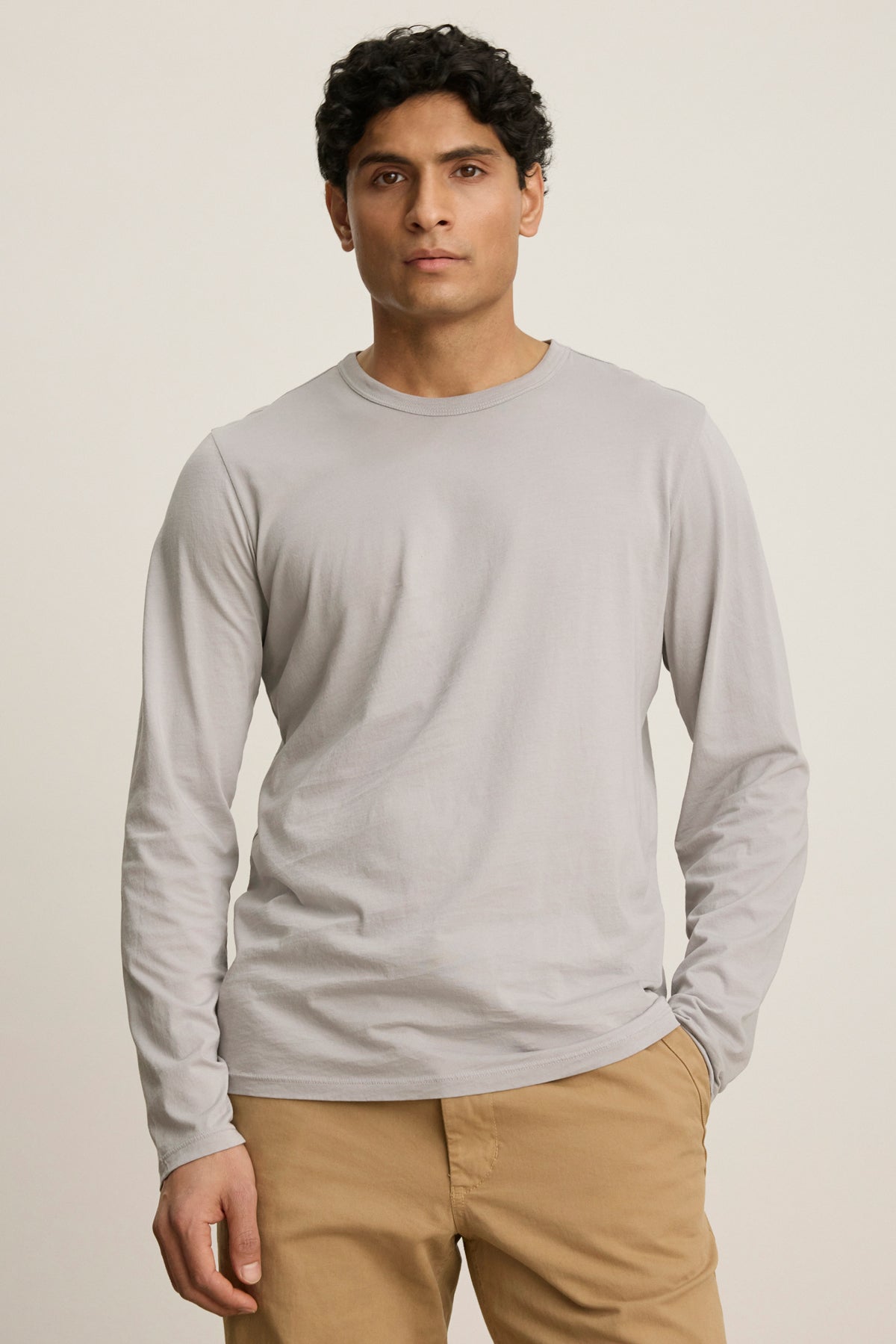 A man wears the ROWLAND TEE by Velvet by Graham & Spencer in light gray with beige pants, standing against a plain, light-colored background.-39841090339009