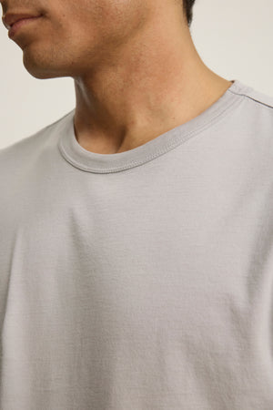 Close-up of a person wearing the ROWLAND TEE by Velvet by Graham & Spencer in light gray Pima jersey, highlighting the soft crew neckline and upper chest. The person's face is partially out of frame.