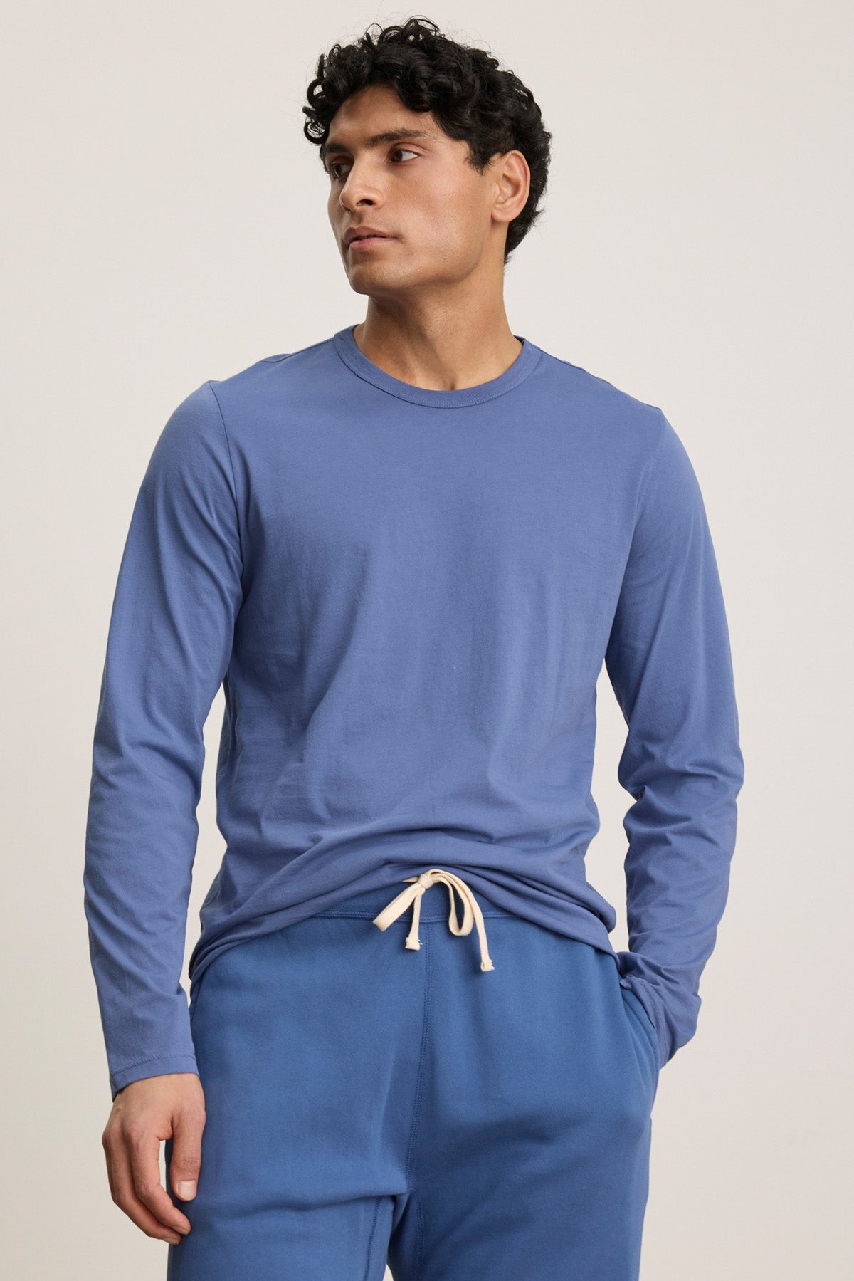 A man wearing the ROWLAND TEE by Velvet by Graham & Spencer and blue drawstring pants stands against a plain light background, looking to the side.-40606036984001