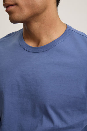 A person wearing the ROWLAND TEE by Velvet by Graham & Spencer in blue, shown from the shoulders up and facing slightly to the left.