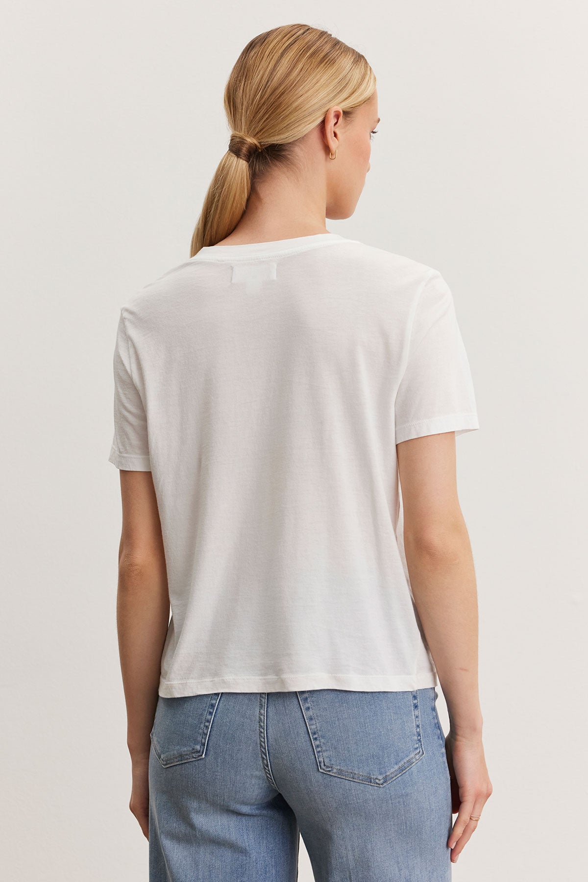 Rear view of a woman with a ponytail wearing a Velvet by Graham & Spencer RYAN TEE in whisper cotton fabric and blue jeans, standing against a light background.-36998721831105