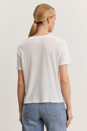 Rear view of a woman with a ponytail wearing a Velvet by Graham & Spencer RYAN TEE in whisper cotton fabric and blue jeans, standing against a light background.