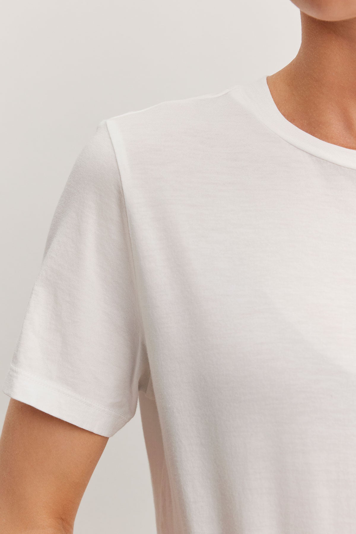   Close-up of a person wearing a Velvet by Graham & Spencer RYAN TEE in plain white, relaxed fit, focusing on the shoulder and sleeve area. The background is neutral. 