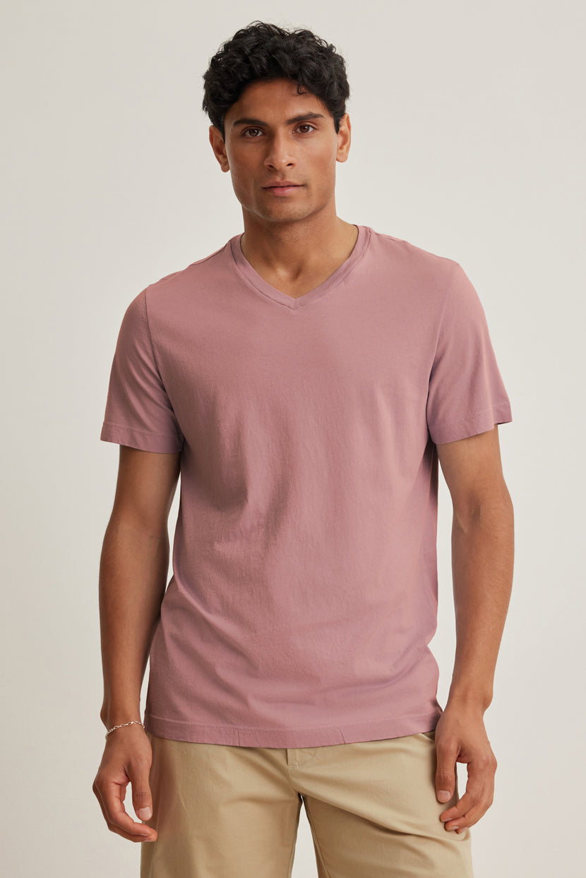 A man faces forward in a Velvet by Graham & Spencer SAMSEN TEE, a short-sleeve mauve Pima jersey V-neck, paired with beige pants against a plain light background.