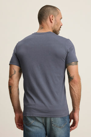 A short-haired, tattooed man in a Velvet by Graham & Spencer SAMSEN TEE—a gray Pima jersey with a subtle V-neck—pairs it with jeans as he faces away.