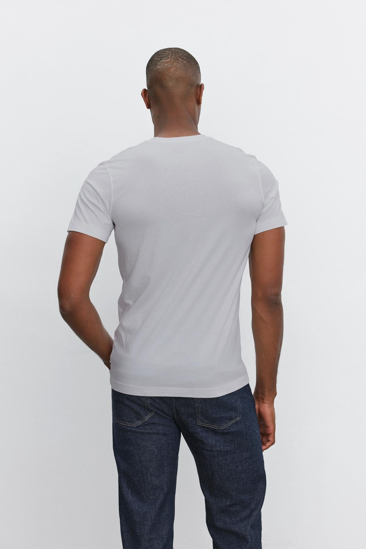   Man wearing a Velvet by Graham & Spencer SAMSEN TEE with a v-neckline and dark blue jeans, standing with his back to the camera against a plain white background. 