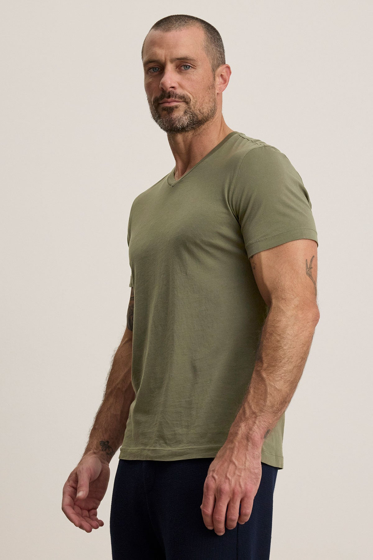 A person in a SAMSEN TEE by Velvet by Graham & Spencer, featuring a green v-neckline and soft Pima jersey, pairs it with dark pants against a plain background, effortlessly showcasing an essential layering piece for any wardrobe.-38670199718081