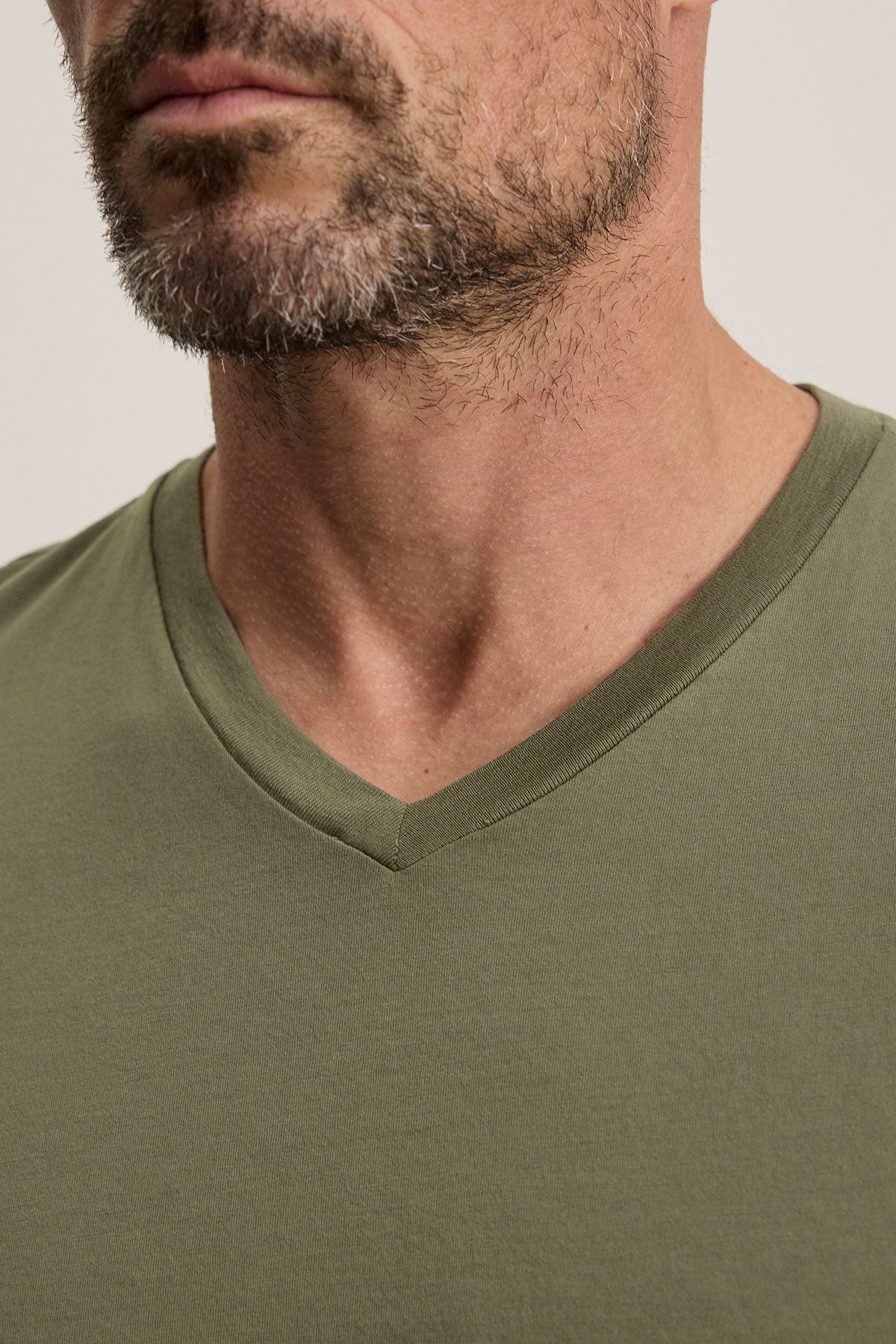 The SAMSEN TEE from Velvet by Graham & Spencer is showcased in a close-up of a man wearing the green Pima jersey V-neck T-shirt. His salt-and-pepper beard adds texture, complemented by a plain light gray background.-38670199750849