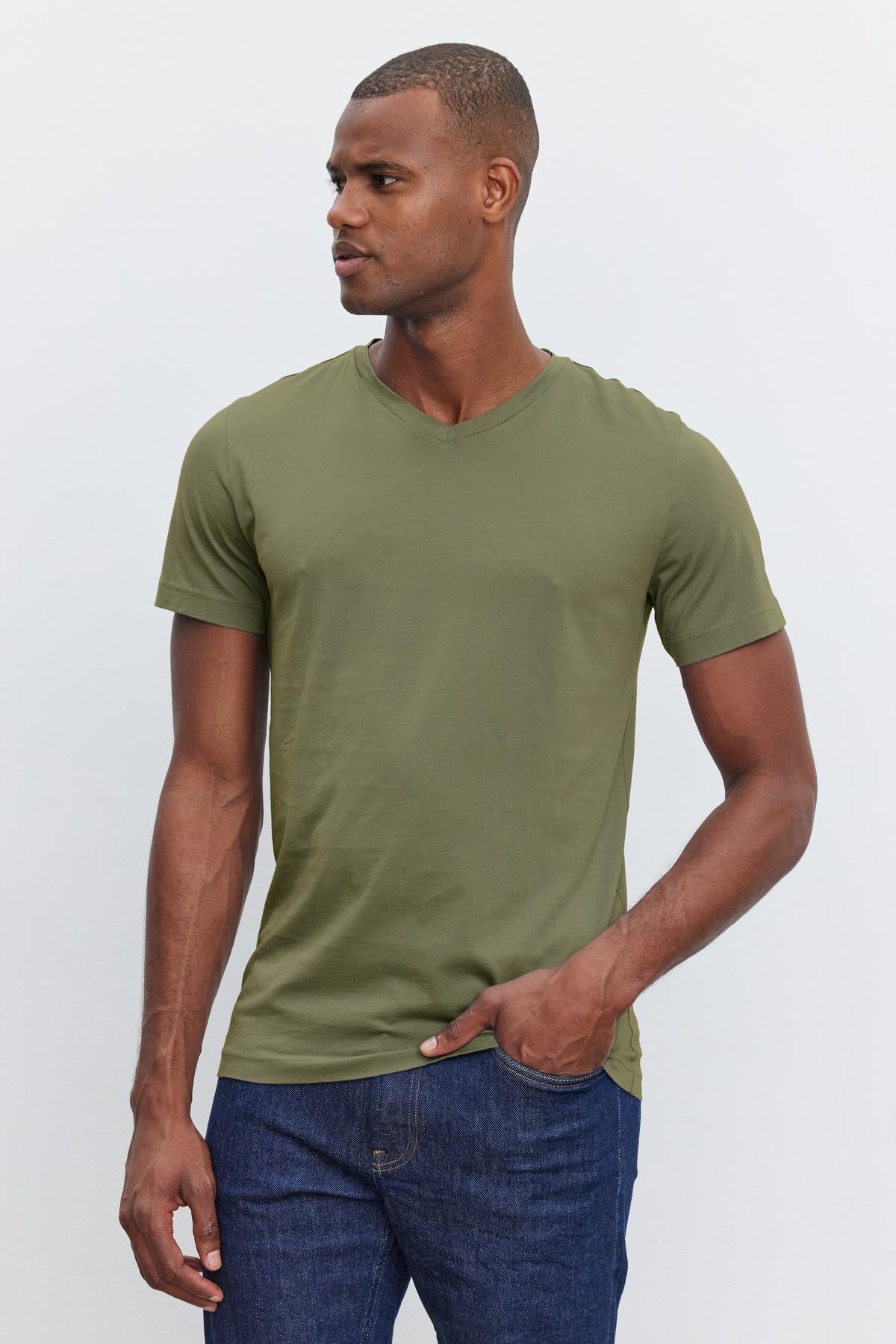 A person wearing the SAMSEN TEE by Velvet by Graham & Spencer, featuring a v-neck and complemented by blue jeans, stands against a plain background, looking to the side and ready for effortless layering.-38264837472449