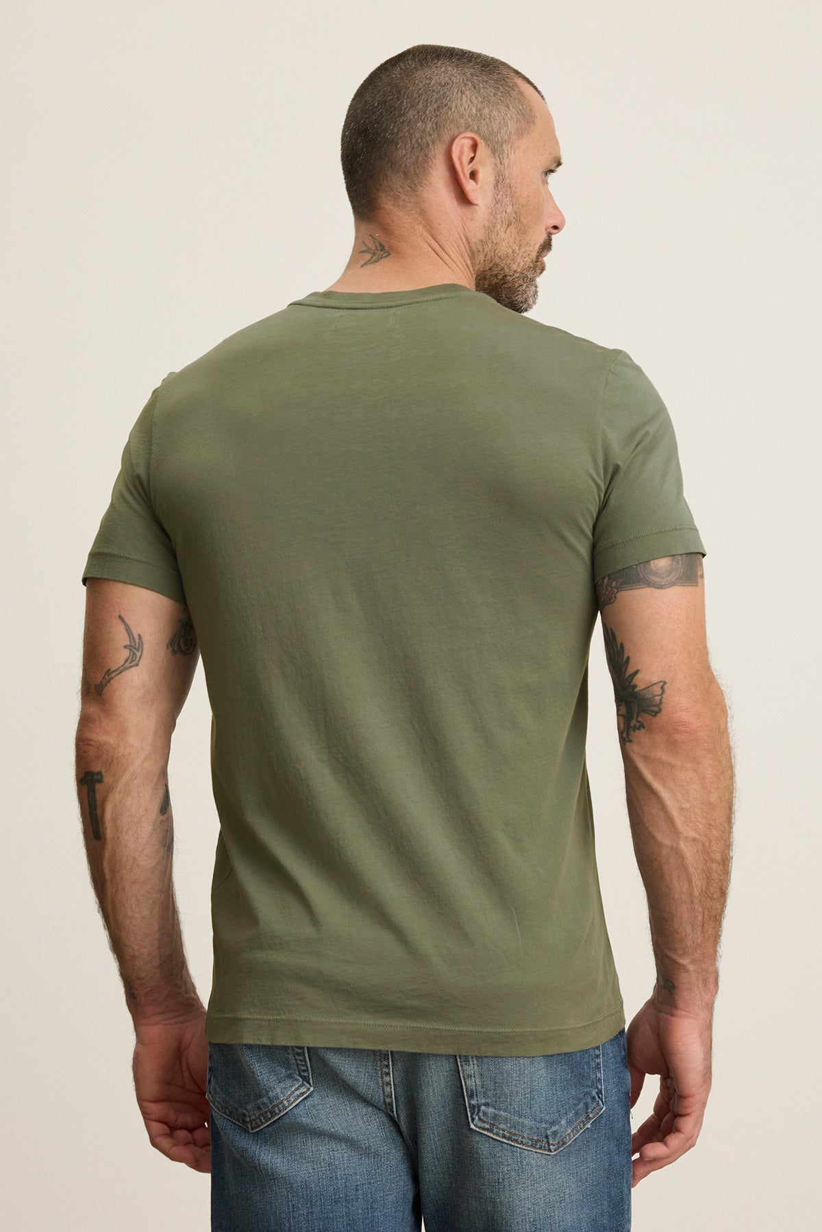   A tattooed man wearing the Velvet by Graham & Spencer SAMSEN TEE in green v-neckline style and jeans, turned away. 