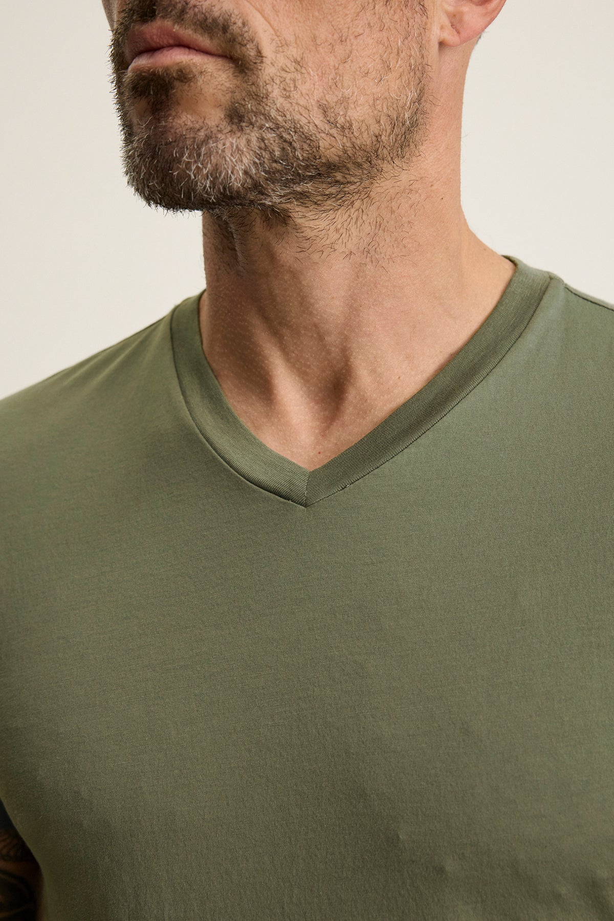   A man with a beard dons the SAMSEN TEE, an olive green V-neck by Velvet by Graham & Spencer, made from soft Pima jersey. 