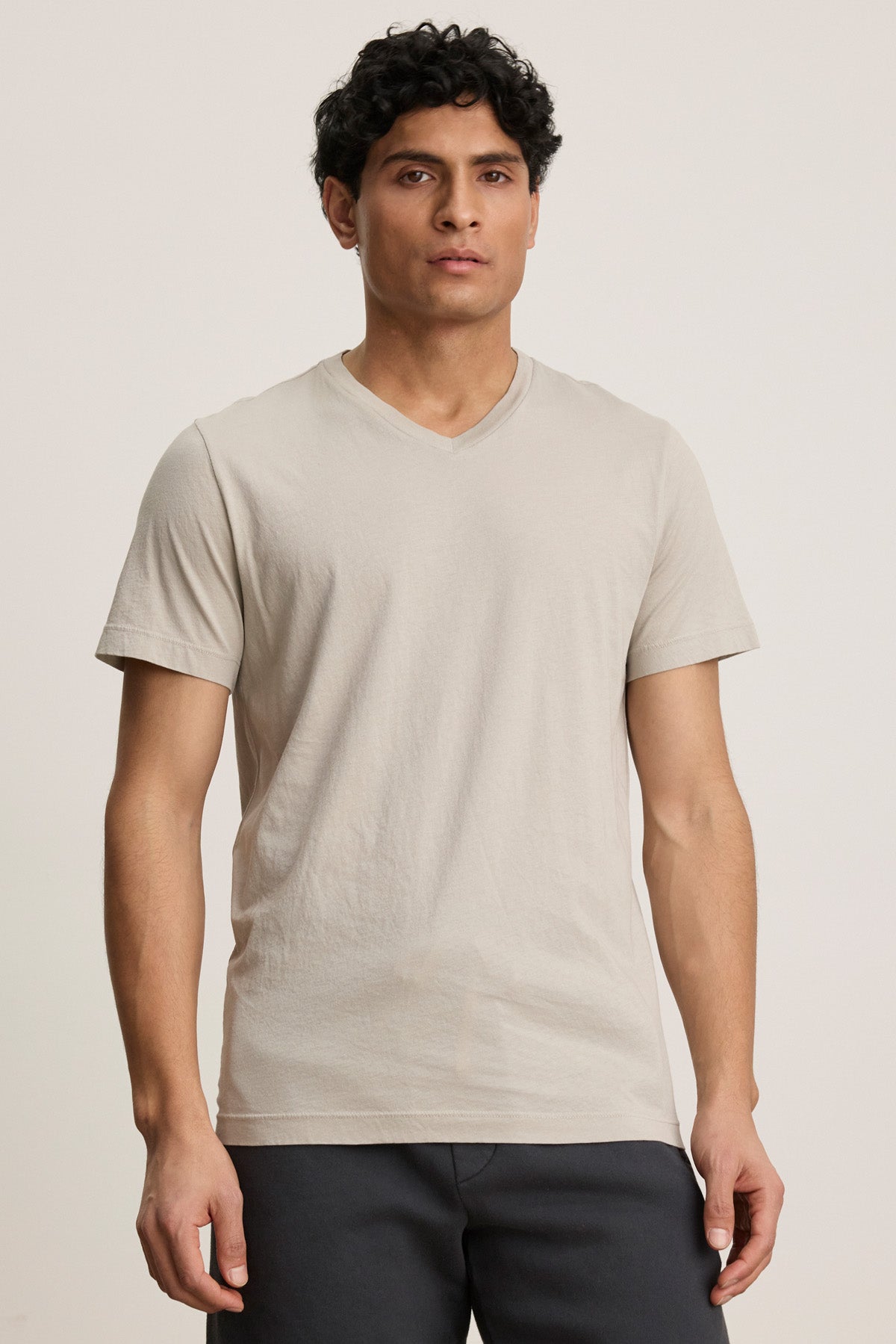 A person faces forward in the SAMSEN TEE by Velvet by Graham & Spencer—a light beige Pima jersey v-neck tee—paired with dark pants against a plain background, ideal for easy everyday style.