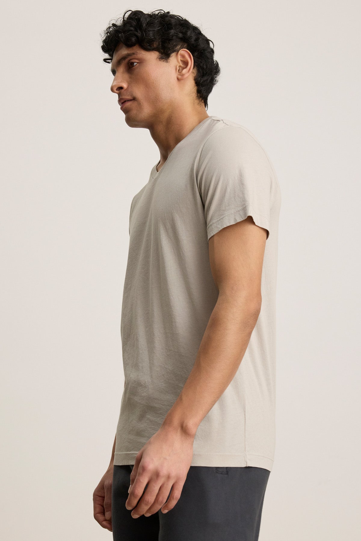 A man stands in profile wearing the Velvet by Graham & Spencer SAMSEN TEE, a plain light beige Pima jersey short-sleeve t-shirt, and dark pants against a neutral background.-40606051172545