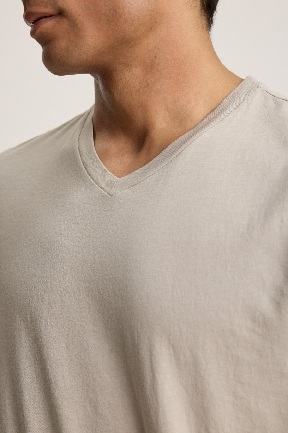A close-up of a person wearing the SAMSEN TEE by Velvet by Graham & Spencer—a light beige Pima jersey V-neckline tee—highlighting the shoulder, neck, and part of the face, perfect for everyday style.-40606051107009