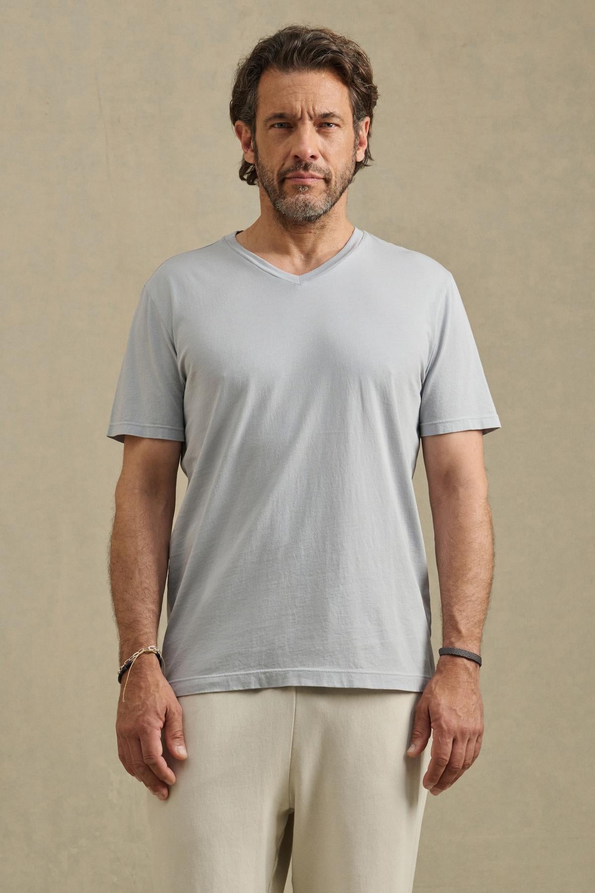 A man with short brown hair and a beard faces forward, wearing the SAMSEN TEE by Velvet by Graham & Spencer in light gray and off-white pants, ideal for everyday wear, against a plain beige background.-41453747896513