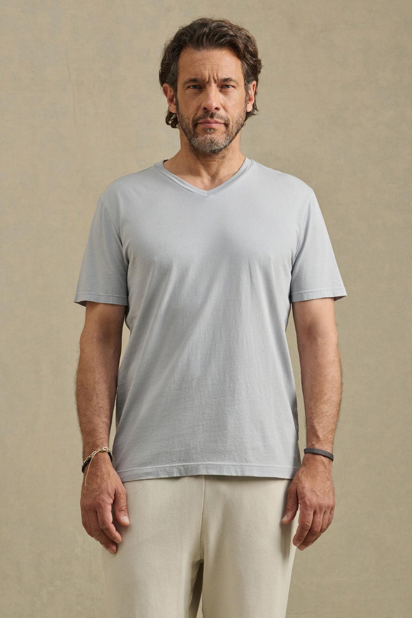 A man with short brown hair and a beard faces forward, wearing the SAMSEN TEE by Velvet by Graham & Spencer in light gray and off-white pants, ideal for everyday wear, against a plain beige background.