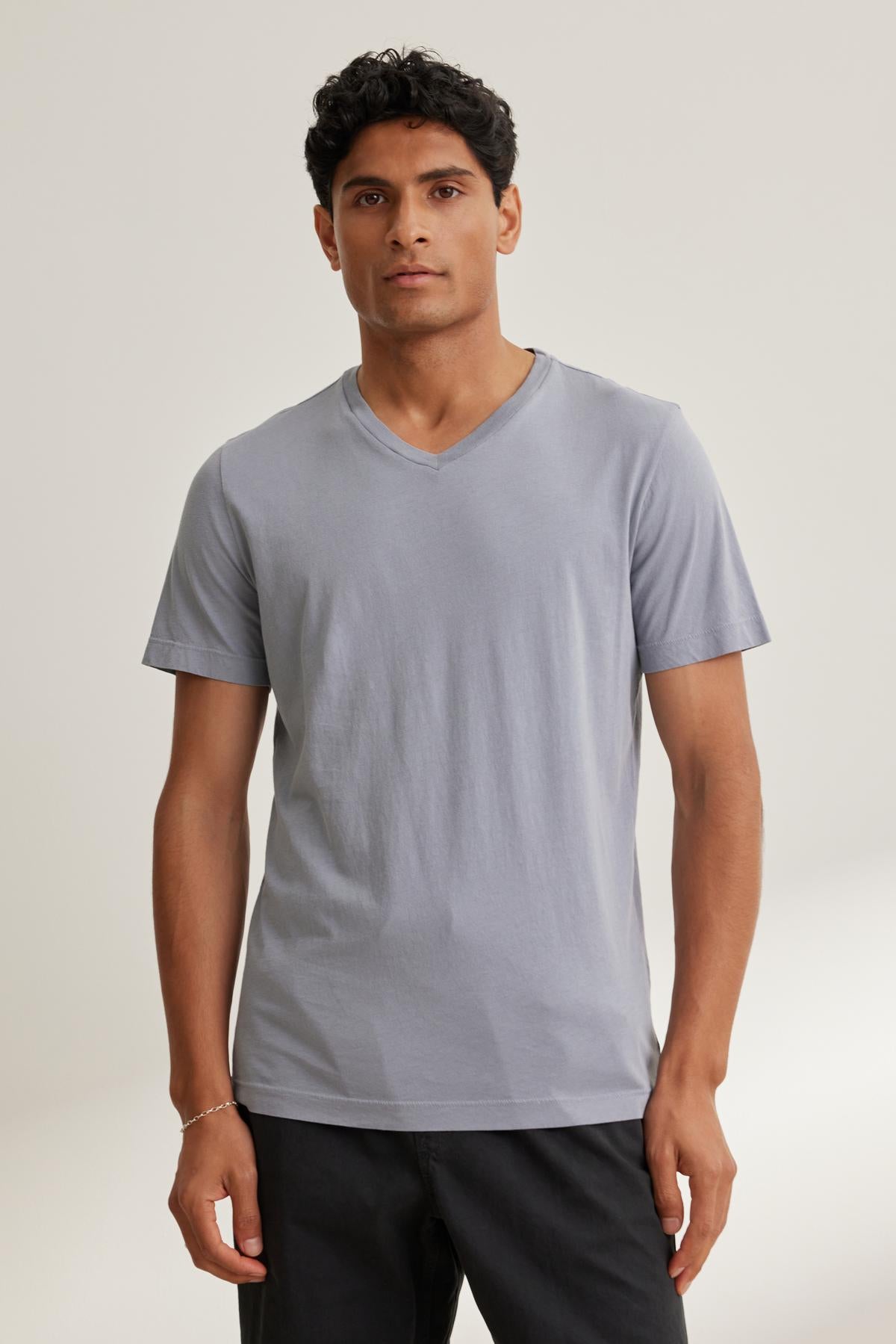 A person wearing a light gray SAMSEN TEE by Velvet by Graham & Spencer paired with black pants stands against a simple background.-38643347128513